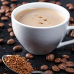 a cup of coffee on a table with sprinkled coffee beans